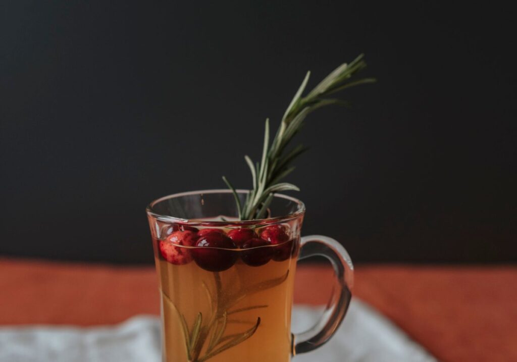 Apple cider shrub mocktail with a rosemary sprig and fresh apples